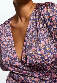 Abito floreale viola con maniche a sbuffo e scollatura a V profonda. Presenta piccoli motivi floreali rosa e oro su un tessuto testurizzato.