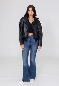 Schwarze Lederjacke mit Kapuze, mit einem Reißverschluss und gerippten Bündchen, kombiniert mit blauen Schlagjeans und weißen Sneakern.