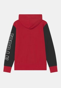 Czerwona bluza z kapturem z czarnymi rękawami, kieszenią kangurką oraz wyraźnym białym logo na lewym rękawie. Miękka tkanina o gładkiej fakturze.