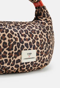 Schultertasche aus Leopardenmusterstoff mit einem weißen Etikett, das das Logo "UNIO Hamburg x Les Visionnaires" zeigt.