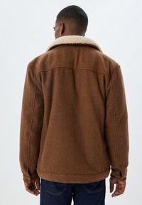 Brown wool-blend jacket with a cream shearling collar, featuring a smooth texture and a buttoned cuff detail. Rear view shows simplicity of design.