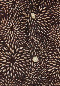 Kortärmad skjorta i mörkbrunt tyg med krämfärgad bladmönster. Har en knäppning och synliga sömnadsdetaljer.