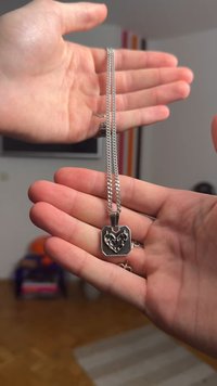 Strieborný náhrdelník so srdcovým príveskom s prepracovaným vyrezávaným dizajnom, zavesený na hrubom retiazku, držený v ruke na vystavenie.