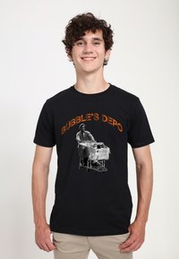 Sort bomulds T-shirt med grafisk tryk af en mand med indkøbsvogne. "BUBBLE'S DEPO" teksten i orange buer over billedet.
