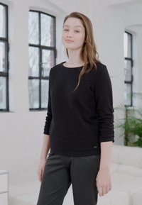 Zwart getextureerd langemouwen shirt gecombineerd met donkergrijze broek. Het shirt heeft een ronde halslijn en lijkt zacht met subtiele details.