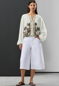 Culottes blanches amples et une blouse blanche avec un imprimé de palmiers noir et marron, boutons détaillés et manches bouffantes.