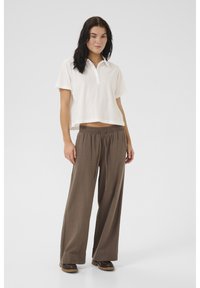 Witte cropped polo met een knoopcol, gecombineerd met bruin wijde broek met een elastische tailleband en trekkkoord.