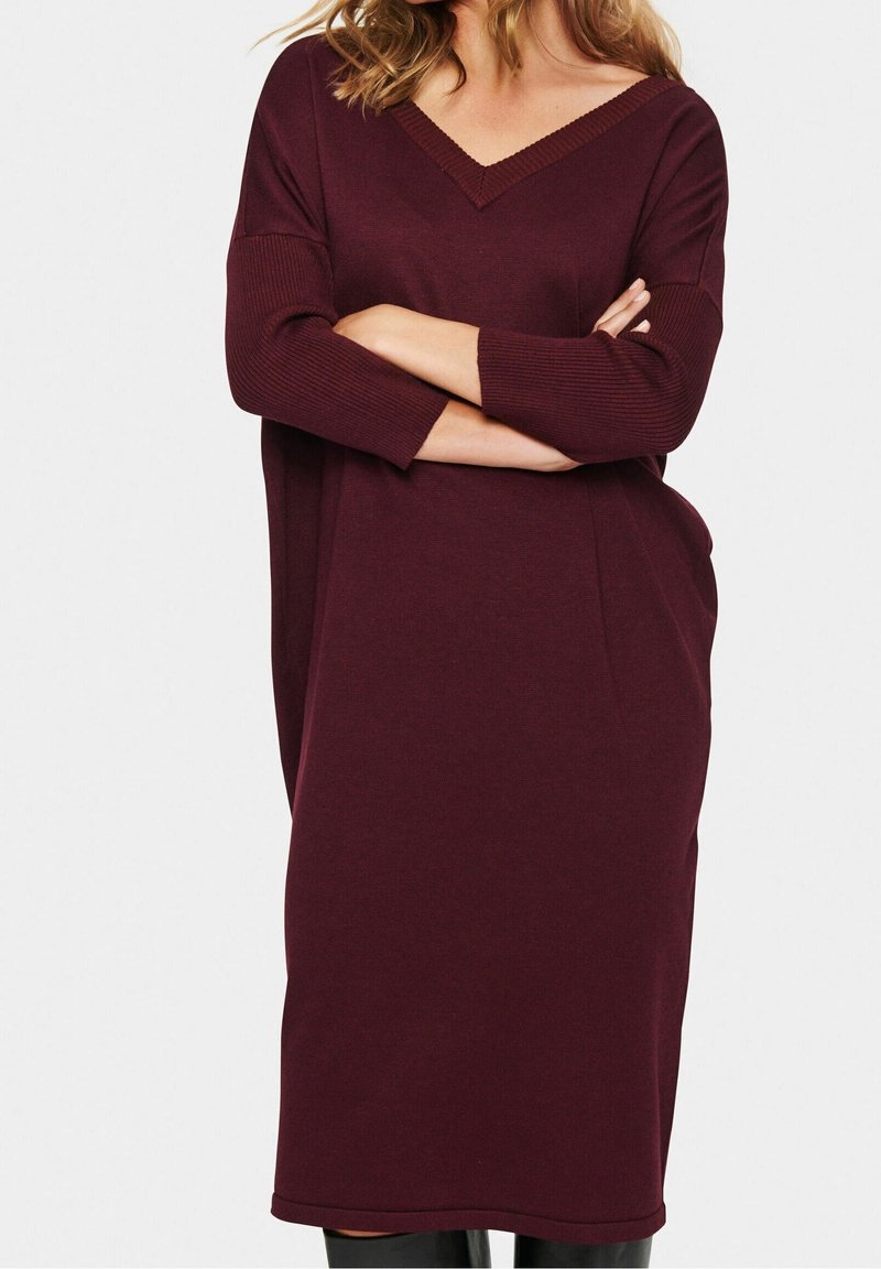 Robe en maille bordeaux avec col en V, manches trois-quarts et coupe décontractée, présentant des détails côtelés le long du col et des manches.