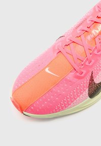 Chaussure de sport rose et orange avec le logo Nike, tige en maille et lacets, vue en plongée inclinée.
