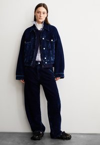 Mörkblå kordjacka med stora fickor och framknäppning, ihopkopplad med matchande vida kordbyxor, som har en texturerad yta och lös passform.