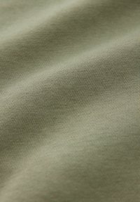 Gros plan d’un tissu vert olive lisse avec une texture en maille fine et des variations subtiles de lumière et d’ombre sur la surface.