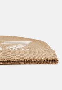 Beanie in maglia color beige con orlo ripiegato e motivo testurizzato; design del logo bianco integrato nella superficie.