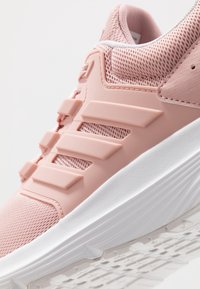 Zapatilla deportiva rosa con parte superior de malla transpirable, detalles de plástico y suela de goma blanca con un patrón texturizado.