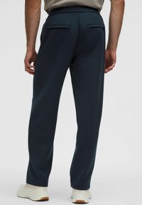 Marineblå, tapered bukser med en blød tekstur, elastisk talje og to baglommer. Kombineret med lyse sneakers.