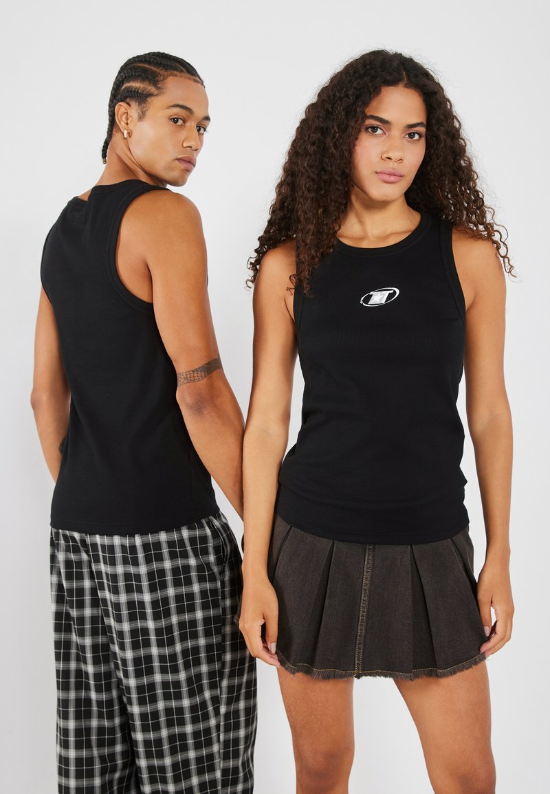 Hauts noirs sans manches en tissu côtelé, chacun présentant un petit logo. Un modèle porte un pantalon à carreaux, l'autre une jupe plissée en denim.