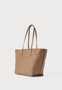 Τσάντα tote σε καφέ χρώμα με δύο δερμάτινες λαβές, ορθογώνιο σχήμα, μίνιμαλ σχεδιασμός και αντίθετη ραφή κατά μήκος των ακμών.