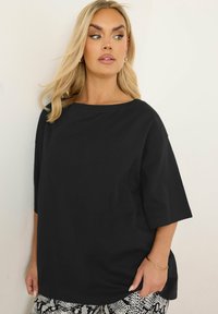 Svart, oversized t-shirt med vid halsringning och korta ärmar, tillverkad av ett mjukt material. Bärs med mönstrade, högmidjade byxor.