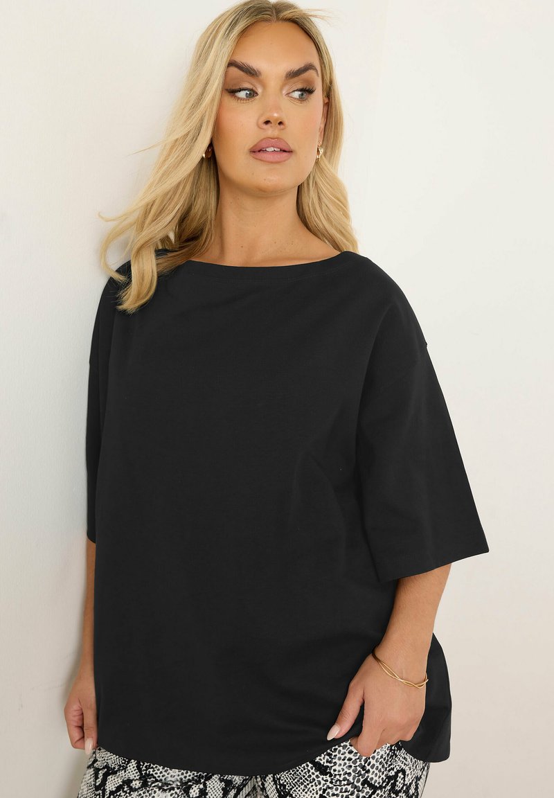 Svart, oversized t-shirt med vid halsringning och korta ärmar, tillverkad av ett mjukt material. Bärs med mönstrade, högmidjade byxor.