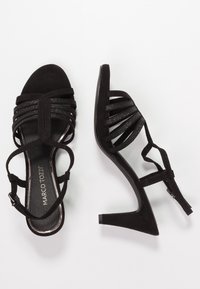 Czarne zamszowe sandały na wysokim obcasie z wieloma wąskimi paskami i regulowanym zapięciem wokół kostki, z teksturowaną wkładką wewnętrzną i zwężającym się obcasem.