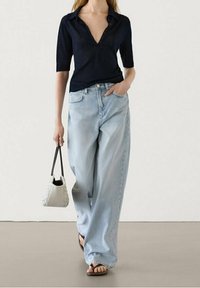 Mørkeblå kortærmet polo shirt med knaplukning. Bæres sammen med lyseblå vidde jeans og en lille hvid håndtaske. Flade sandaler.