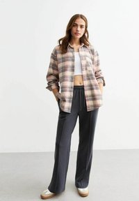 Hellblau gestreiften Button-Up-Hemd in den Farben Pink und Beige, kombiniert mit dunkelgrauen Jogginghosen und beigen Turnschuhen. Glatte Textur, bequemer Schnitt.