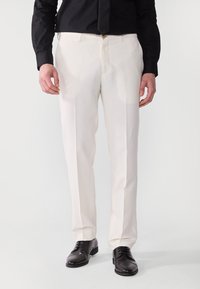 Hellgraue maßgeschneiderte Hose mit einer glatten Textur, geradem Beinprofil und dezentem Glanz, kombiniert mit schwarzen Dressschuhen.