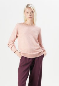 Light pink sweater with a round neckline, ribbed cuffs, and bottom hem, worn over dark purple pants. Soft texture, casual fit.
