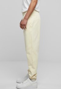 Light yellow sweatpants made of soft fabric, featuring a ribbed waistband, side pockets, and elastic cuffs. Worn with white sneakers.