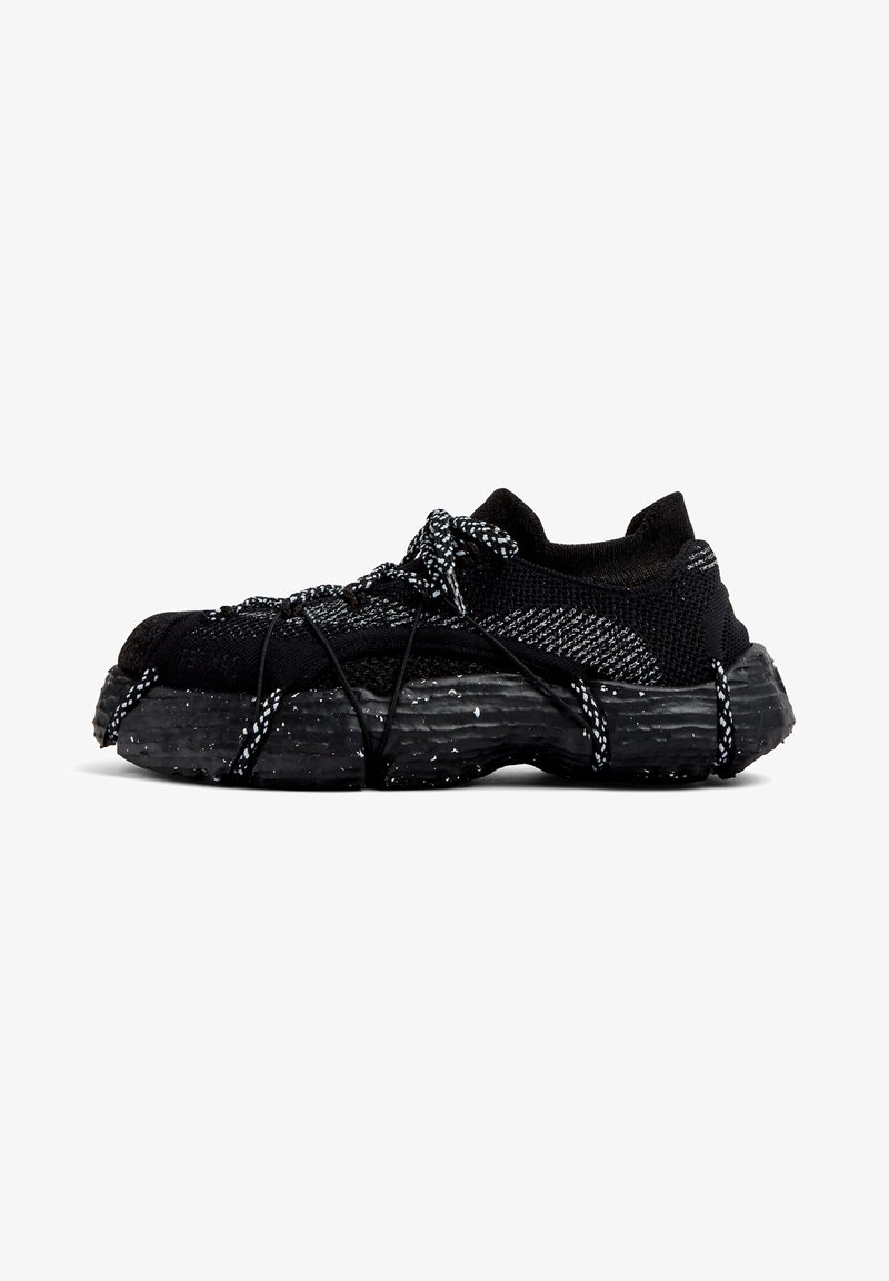 Black athletic shoes with a textured synthetic upper and speckled black rubber outsole. Features elastic laces and a low-cut design.