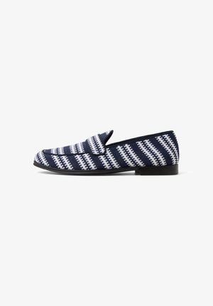 Mocassins tissés bleu marine avec un motif géométrique blanc, semelle plate noire et forme allongée. Présentent un bout rond et aucun matériel visible.