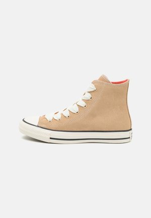 Hochschaft-Sneaker aus weichem beigem Wildleder, mit weißen Schnürsenkeln, einer runden Zehenform, schwarzen Streifen entlang der Sohle und einem kontrastierenden roten Innenfutter.