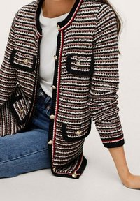 Gestrickte Strickjacke in Schwarz, Weiß und Rot mit gestreiftem Muster. Verfügt über zwei Fronttaschen und goldfarbene Knöpfe entlang des Verschlusses.