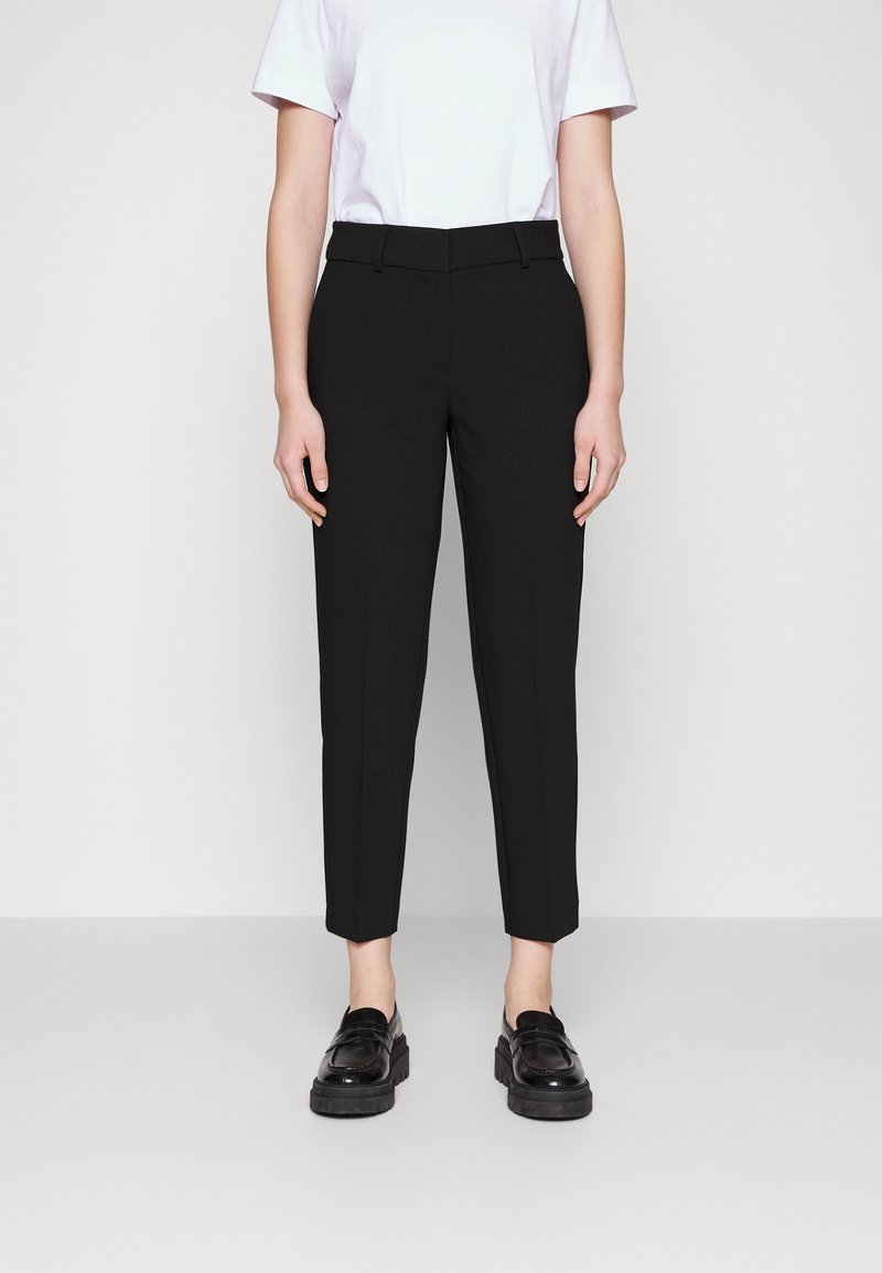Pantalons noirs adaptés avec une coupe slim, présentant un devant plat, des poches latérales et une longueur raccourcie. Associés à des mocassins en cuir noirs.