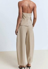 Beige strapless top en wijde broek gemaakt van een gladde stof. Opvallende tatoeage op de rug, met dunne banden op de schoenen.