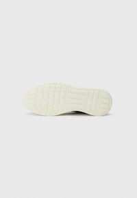 Shoe sole with a textured pattern, predominantly white with a grid design. Rounded edges and a smooth finish, indicating flexible material.