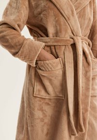 Beżowy pluszowy szlafrok z kołnierzem szalowym, przewiązany pasującym paskiem. Posiada dwie przednie kieszenie o miękkiej, teksturowanej powierzchni. Miękka tkanina.