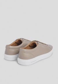 Zapatillas de cuero beige con un acabado suave, que cuentan con suelas de goma blanca, cordones redondos y forro de cuero marrón claro. Diseño limpio y minimalista.