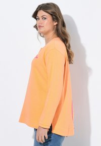 Langarm-Sweatshirt aus leuchtend orangefarbenem Baumwollstoff. Mit einem runden Halsausschnitt und leichten seitlichen Schlitzen. Akzentuiert mit pinkem Design auf der Brust.