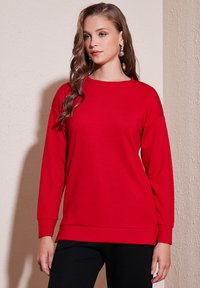 Felpa rossa a maniche lunghe con scollo rotondo, polsini rigati e vestibilità comoda. Realizzata in tessuto morbido, presenta una texture liscia.