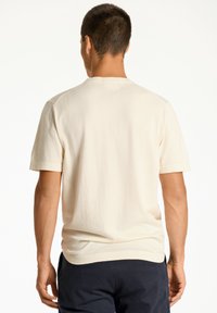 Krämfärgad T-shirt med kort Ärmar i ett mjukt tyg, med rund halsringning, sömlös axeldesign och rak fåll, bärs tillsammans med mörka byxor.