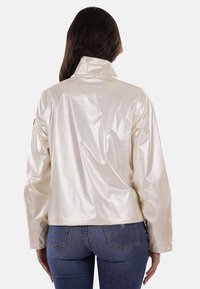 Giacca bianca, lucida e impermeabile, con un alto collo, spalle drop e cuciture minime. Presenta tasche laterali e una patch con logo sulla manica.