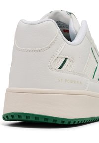 Vit lädersneaker med gröna accenter, texturerad yta, vadderad krage och tan gummisula. Gyllene bokstäver står det "ST. POWER PLAY."