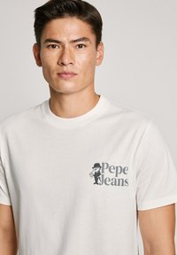 Bílý bavlněný tričko s šedou grafikou postavy v obleku a klobouku s textem "Pepe Jeans" na levé části hrudníku.
