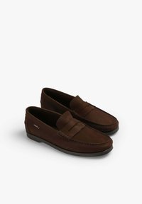 Los mocasines de ante marrón presentan un diseño cosido, un tacón plano y una tira decorativa en la parte superior. El interior está forrado para mayor comodidad.