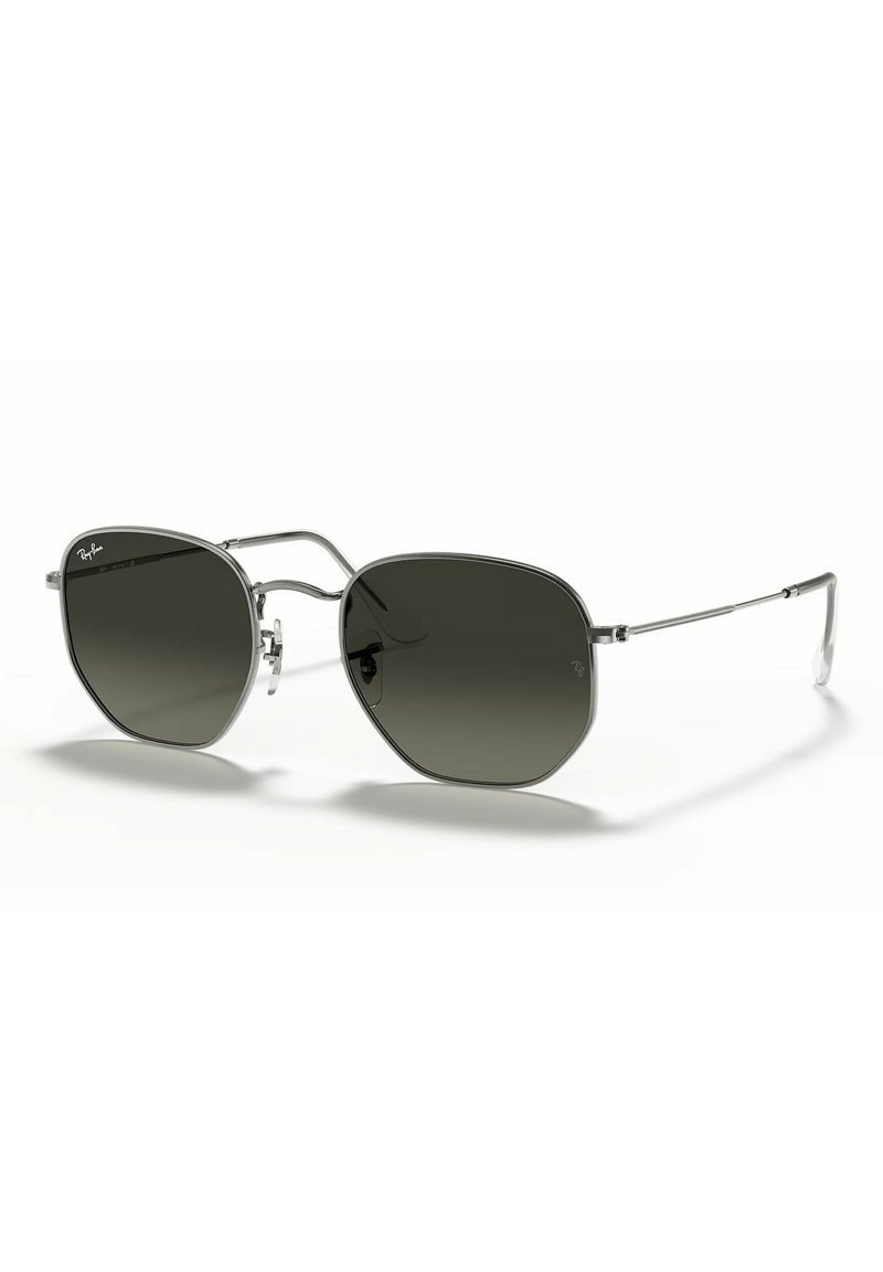 Occhiali da sole aviator argento con lenti grigie scure, caratterizzati da un design unico della montatura ottagonale e da sottili bracci in metallo, sono in mostra.