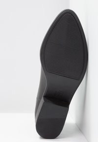 Semelle de chaussure noire en caoutchouc texturé, avec un léger talon et une vue latérale montrant un design avant lisse. Taille imprimée en dessous.