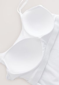 Sottoveste bianca con coppe moldabili, spalline regolabili e morbida fascia elastica. Texture liscia e design senza cuciture, che enfatizza un aspetto pulito e minimalista.