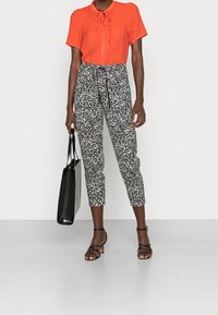 Red textured blouse with a tie neck, paired with black and white patterned cropped trousers. Black tote bag and strappy sandals complete the look.