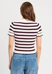 Top à manches courtes rayé en crème, marine et bordeaux. Présente une texture côtelée et une silhouette ajustée avec un col arrondi.