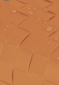 Gewebeoberfläche in Orange mit einem Rautenmuster, das erhabene Bereiche und Wassertropfen auf dem Material aufweist, was der Textur Tiefe verleiht.